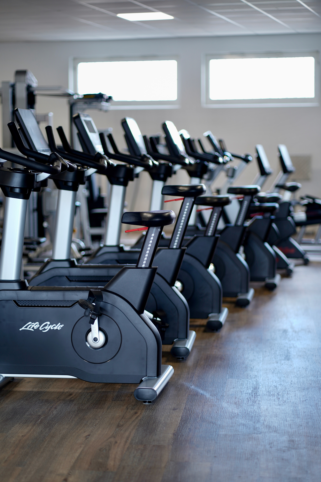Mehrere schwarze Fitnessgeräte stehen ordentlich in einer hellen Sporthalle nebeneinander