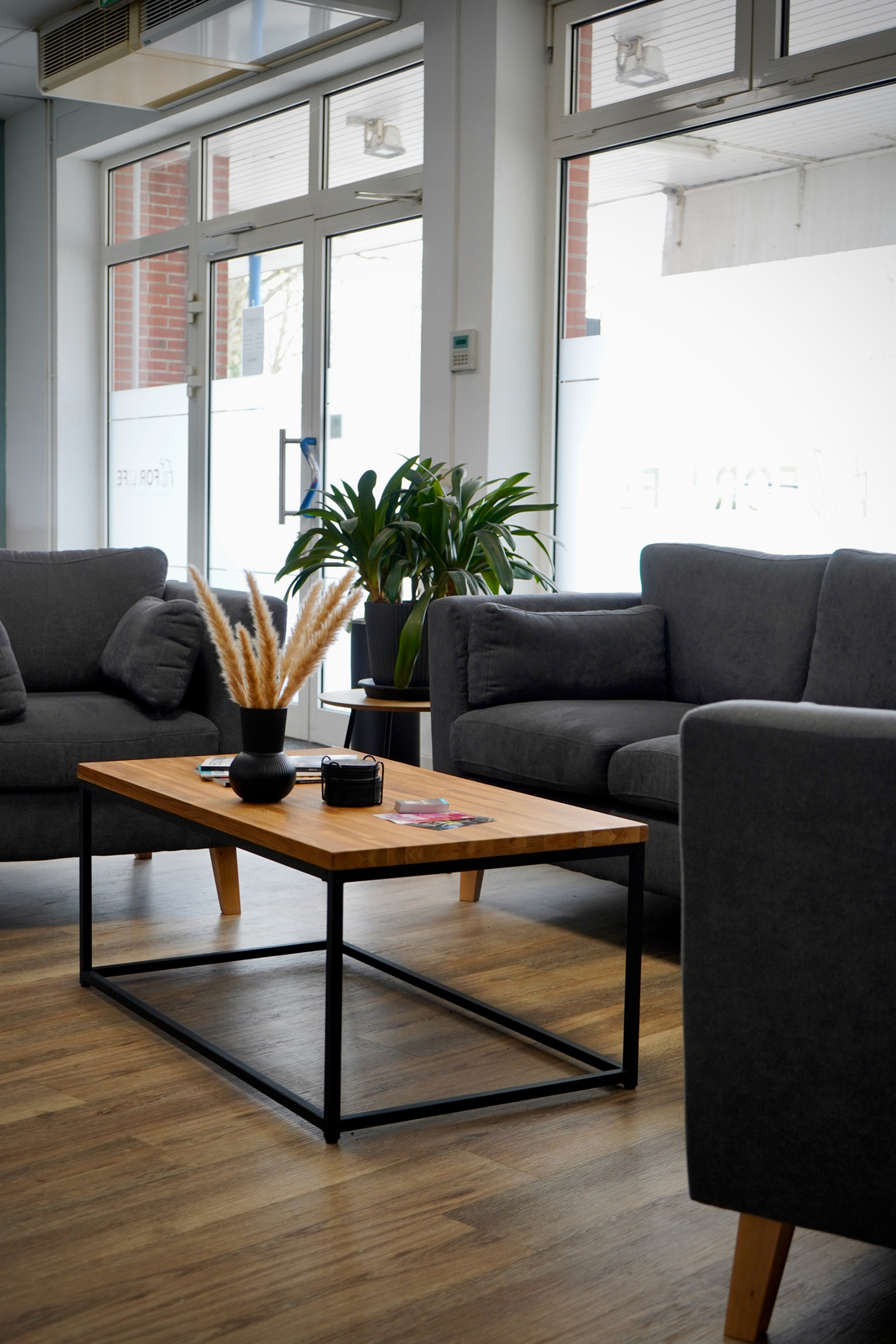 Ein moderner heller Warteraum mit grauen Sofas Holztisch und grünen Pflanzen
