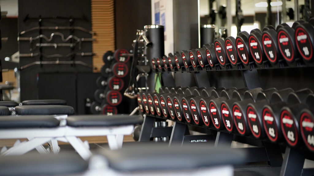Mehrere Hanteln in Schwarz und Rot liegen ordentlich in einem modernen Fitnessstudio