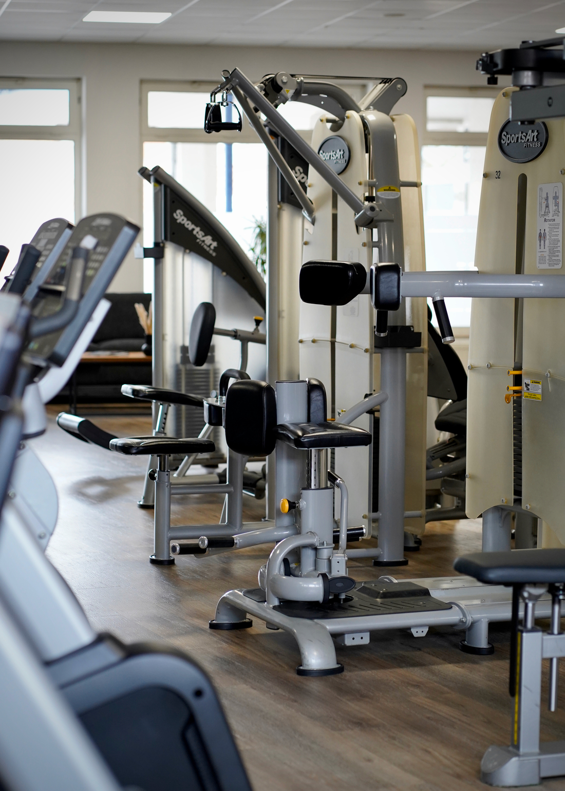 Ein moderner Fitnessraum mit silbernen Trainingsgeräten auf hellem Holzboden
