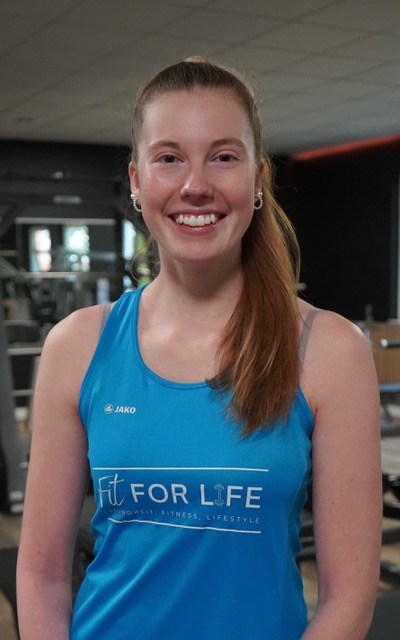 Laechelnde junge Frau im blauen Fit for Life Top im Fitnessstudio